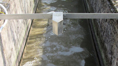 Über einem Rechteckkanal mit fließendem Schmutzwasser ist eine Leiste angebracht. An dieser ist eine Haltevorrichtung montiert mit dem NIVUS Oberflächenradarsensor und einem NIVUS Füllstandssensor.